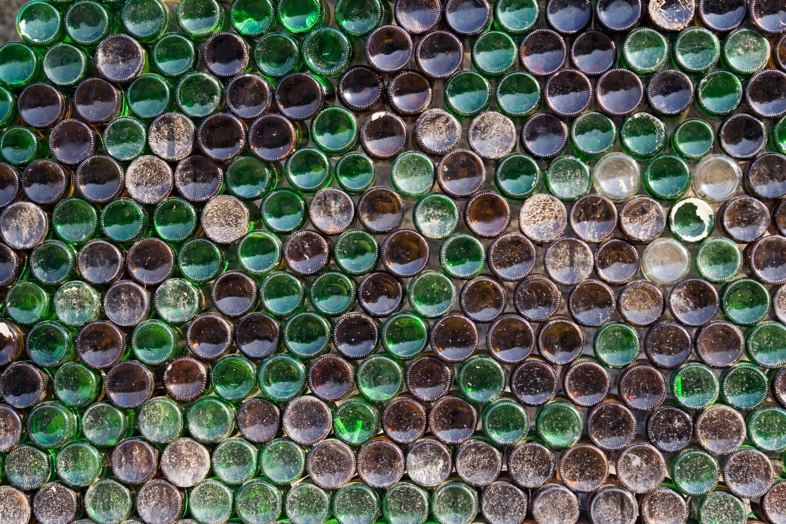 Close-up of green and brown recycled glass bottle bottoms forming an abstract pattern.